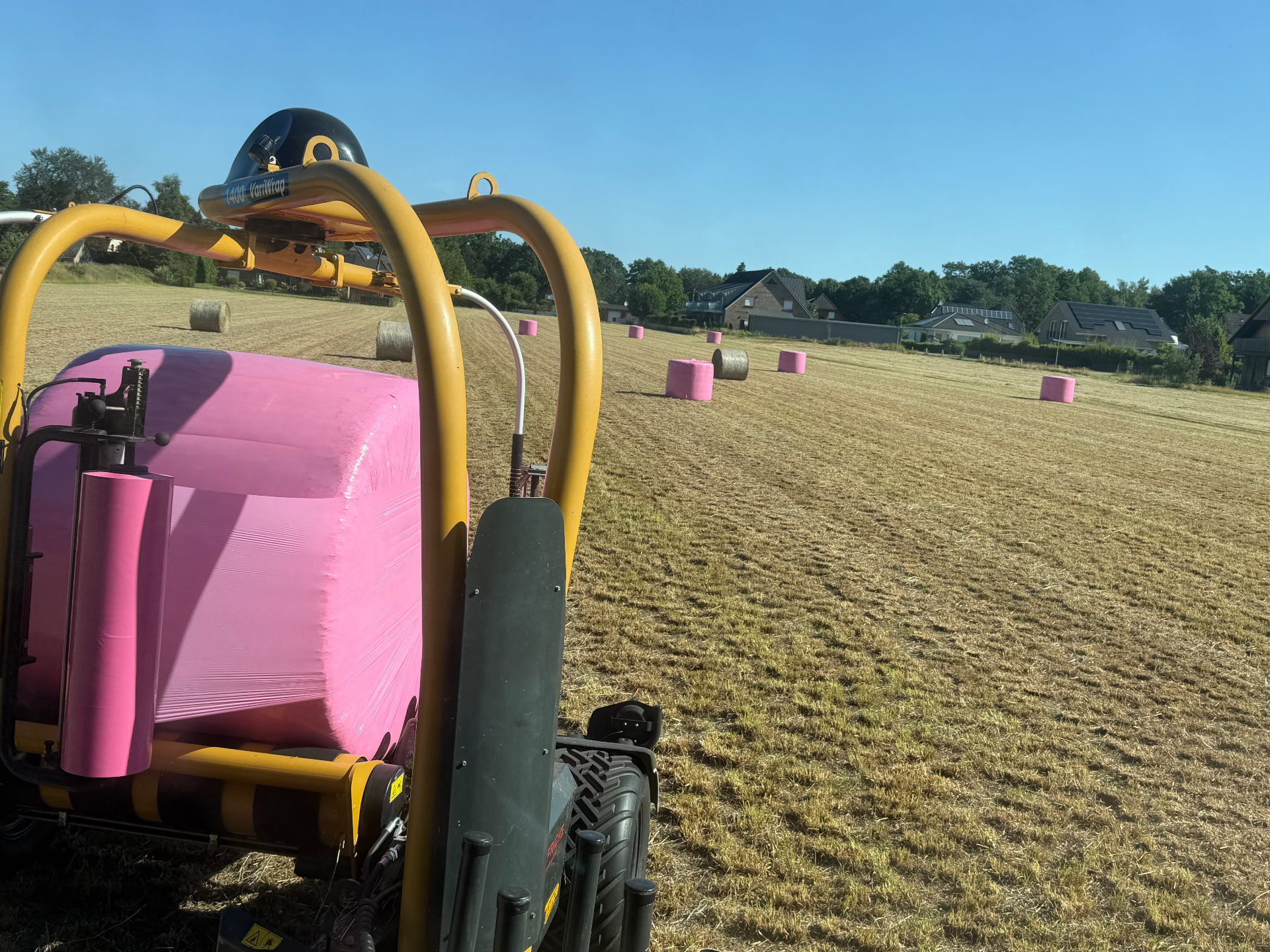 Ballenwickler mit pinker Silageballe auf dem Feld